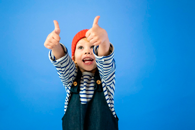 Niño pequeño levantando ambos pulgares con los brazos extendidos, simbolizando confianza y resiliencia emocional, desarrollada desde casa.