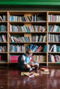 Un niño sentado en el suelo frente a una estantería de libros ilustra las ventajas de la convivencia escolar