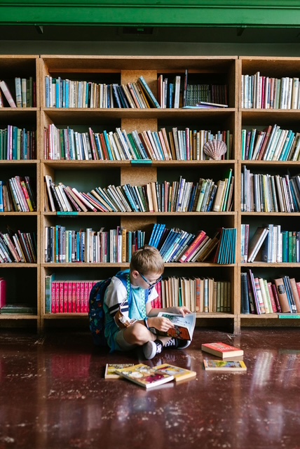 Un niño sentado en el suelo frente a una estantería de libros ilustra las ventajas de la convivencia escolar